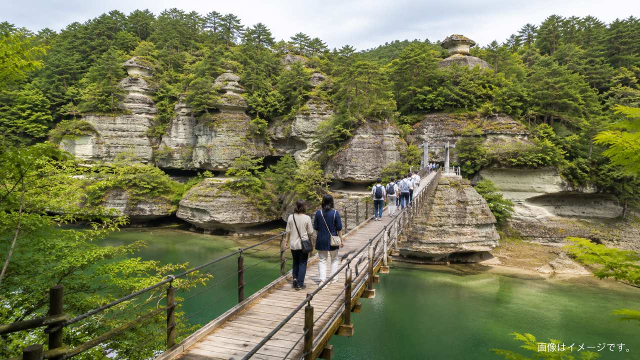 塔のへつりの吊り橋を歩く観光客の後ろ姿を遠景で捉えた実写風画像