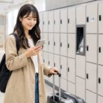 駅のコインロッカーが埋まって困っている旅行者が、スマートフォンで近くの手荷物預かりサービスを検索している実写風写真