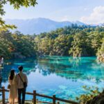 福島県でデートを楽しむ若い日本人カップルの後ろ姿、背景に透明感のある五色沼、会津の城を思わせる白い天守